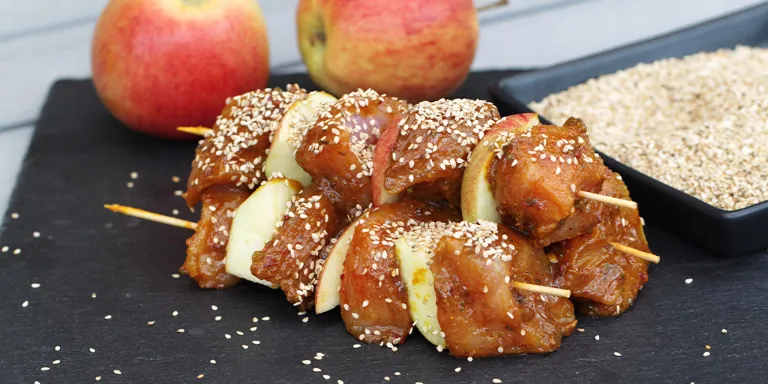 Apfel-Huhn Spieße zum Grillen auf einer Schieferplatte mit ganzen Äpfeln im Hintergrund